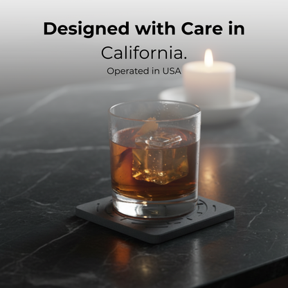 Glass of whiskey with ice on a coaster, candle in the background, text 'Designed with Care in California. Operated in USA'. Sleek stone coasters as a perfect housewarming gift.

