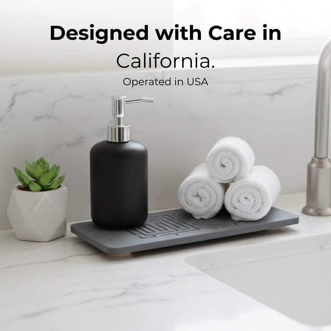 Black soap dispenser on a gray dish rack with white towels and a plant on a marble countertop. The Maze Oasis stone caddy preventing slimy buildup and grime.

