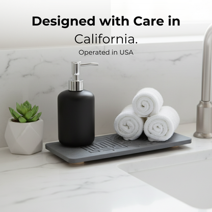 Black soap dispenser on a gray dish rack with white towels and a plant on a marble countertop. The Maze Oasis stone caddy preventing slimy buildup and grime.

