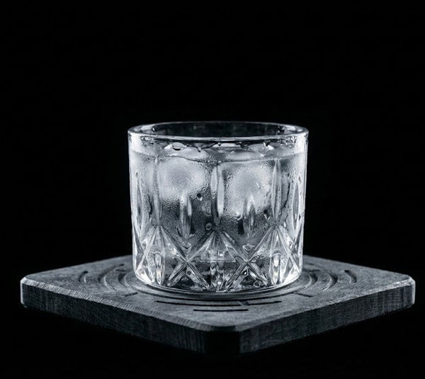 Clear glass with ice cubes on a dark coaster against a black background