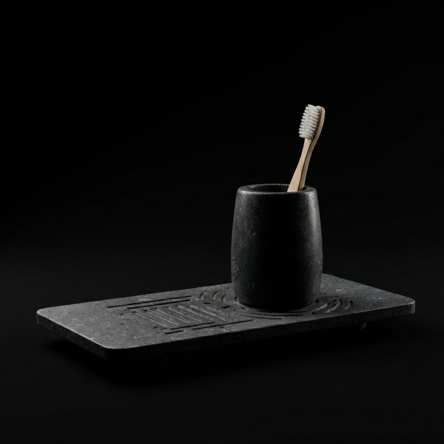 Black ceramic cup with a toothbrush on a matching black tray against a black background