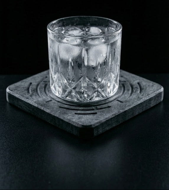 Clear glass with ice on a dark coaster against a black background